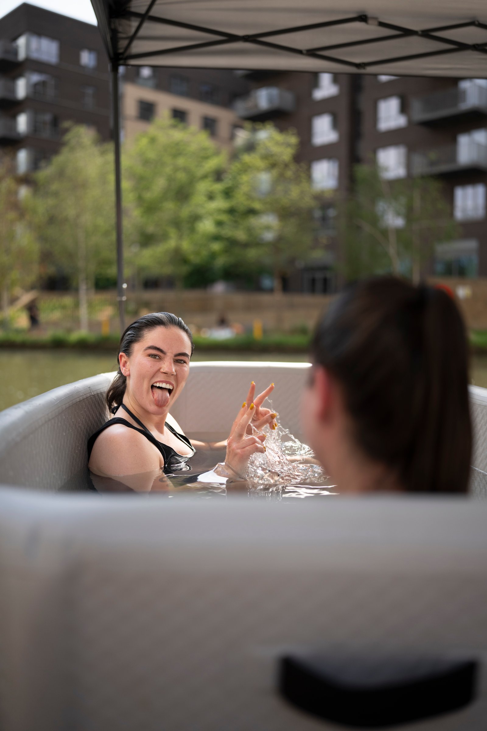 Two women laughing together in an ice bath at a SMÜG garden party